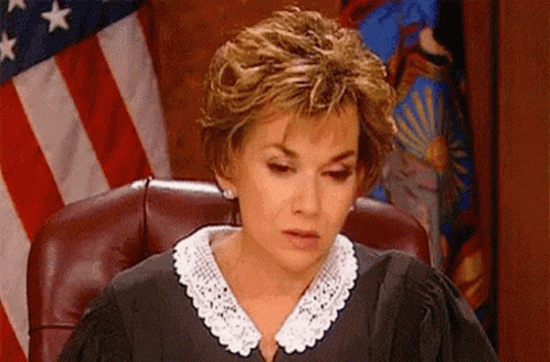 a woman in a judge 's robe is sitting in a courtroom in front of an american flag .