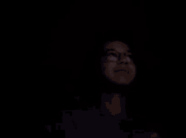 a woman wearing glasses is pointing at something in the dark with her finger .