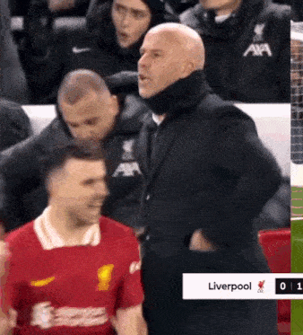 a man in a suit is standing next to a man in a red liverpool shirt