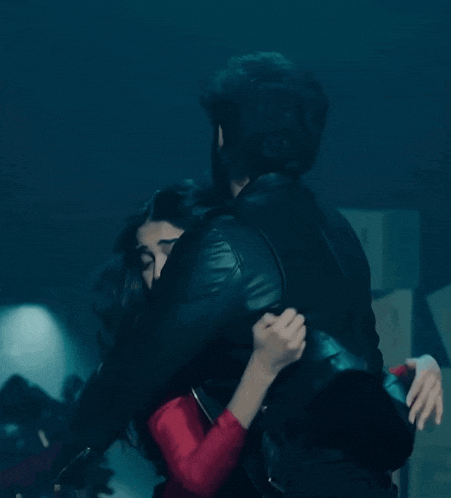a man in a black leather jacket is hugging a woman in a red dress