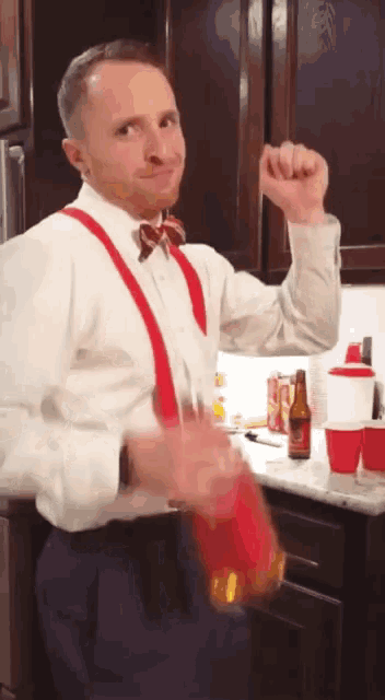 a man wearing red suspenders and a bow tie holds up his fist in the air