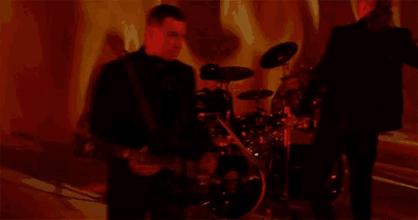 a man in a suit is playing a guitar in front of a drum set