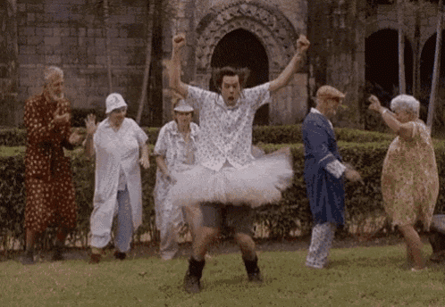 a man in a tutu is dancing with a group of older people in a park .