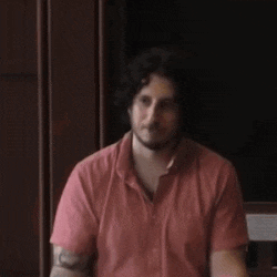 a man in a pink shirt with a tattoo on his arm is smiling and dancing .