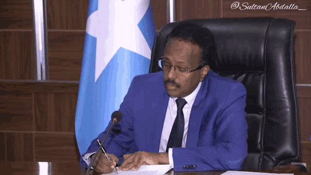 a man in a blue suit sits at a table writing
