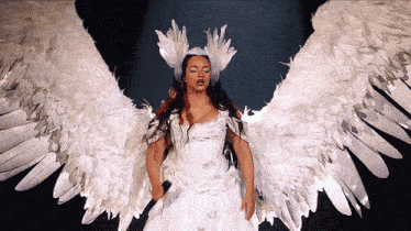 a woman in a white dress with angel wings holds a microphone