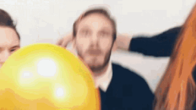 a man with a beard is holding a yellow balloon in front of his face .