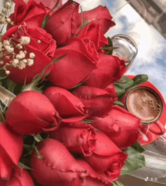 a bouquet of red roses next to a cup of coffee on a table .