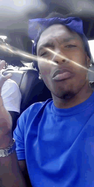 a man wearing a blue shirt and a blue bandana is making a funny face
