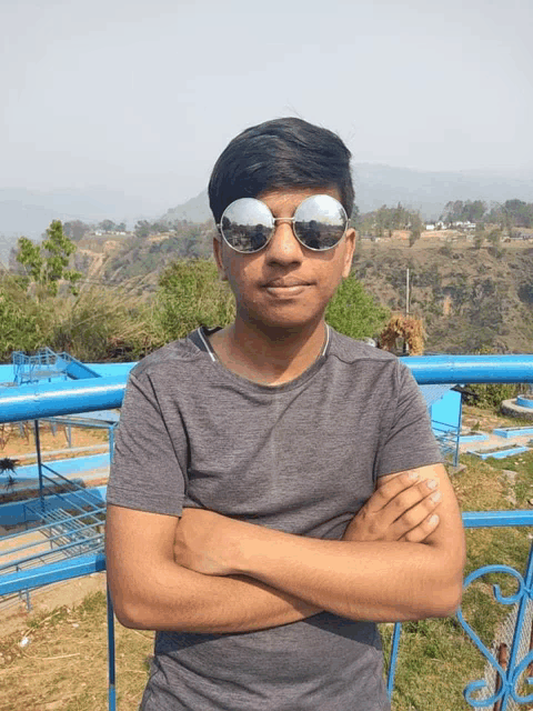 a young man wearing sunglasses stands with his arms crossed in front of a blue railing