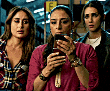 three women are looking at a cell phone in front of a sign that says e