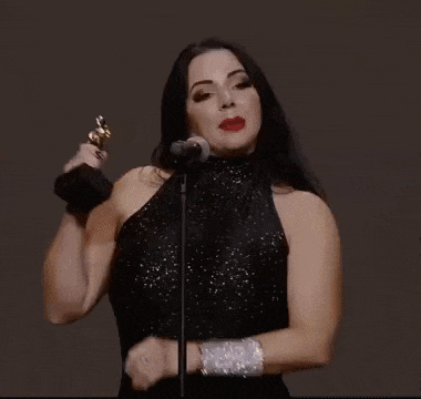 a woman in a black dress is singing into a microphone while holding an oscar .