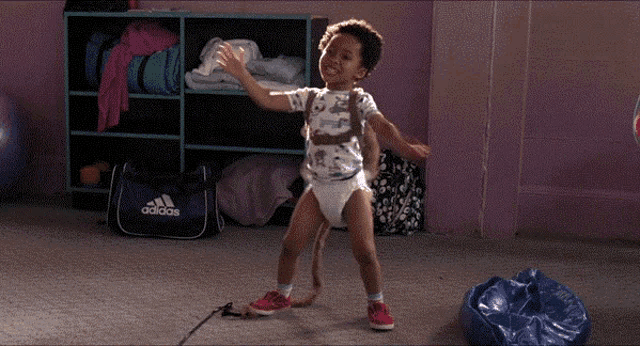 a child in a diaper is dancing in front of a blue adidas bag