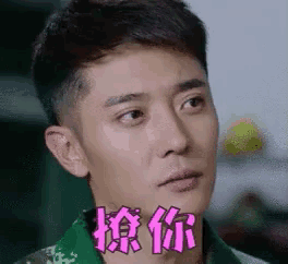 a man in a green shirt is making a funny face with chinese writing on his face .
