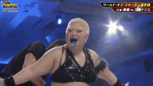 a female wrestler with blonde hair and blue paint on her face is wearing a black bra