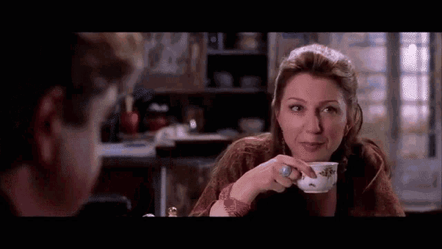 a woman is drinking from a cup while sitting at a table with a boy .