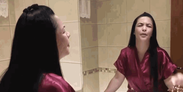 a woman in a red robe is looking at herself in the mirror in a bathroom .