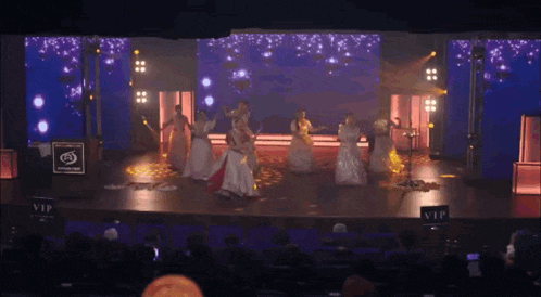 a group of women are dancing on a stage with a sign that says vip in front of them