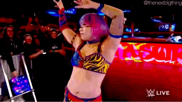 a woman in a wrestling outfit is dancing in front of a crowd in a ring .