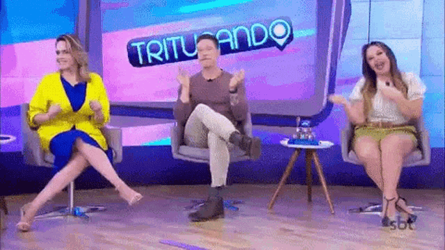 a man and two women are sitting in chairs in front of a television .