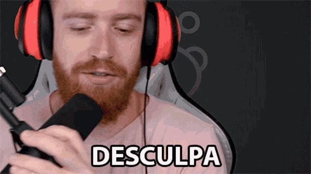 a man with a beard is wearing headphones and holding a microphone with the word desculpa written in front of him .