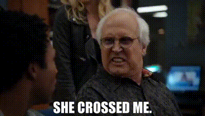 an older man with glasses is sitting in front of a group of people and says `` she crossed me '' .