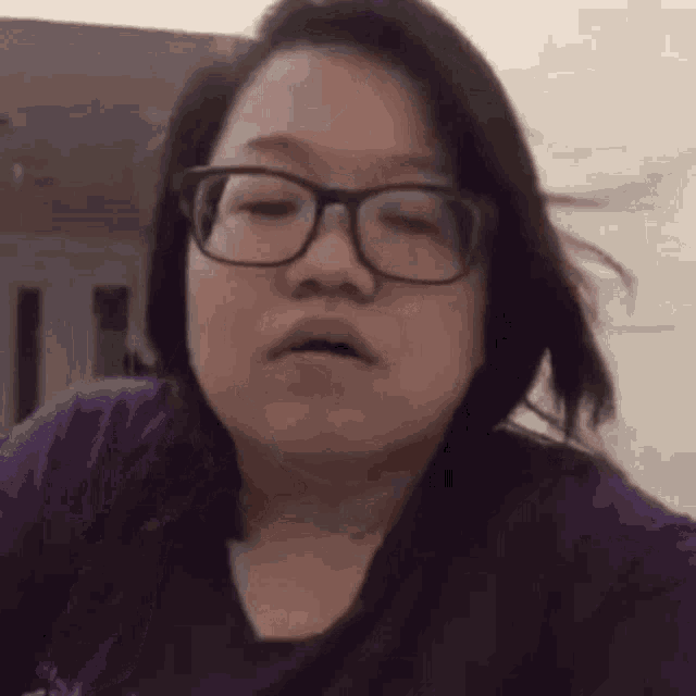 a close up of a woman wearing glasses and a purple shirt making a funny face .