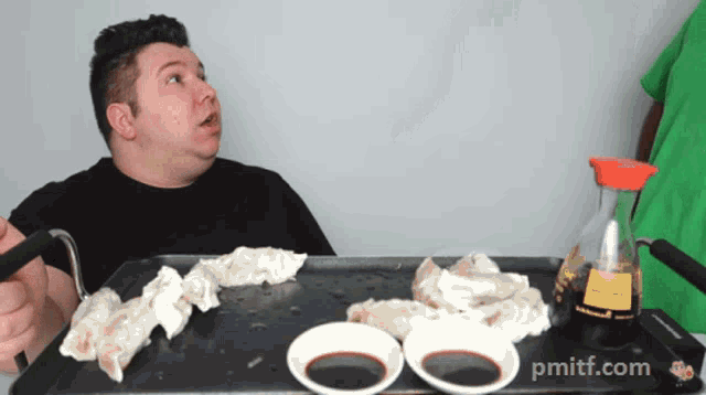 a man sitting at a table with plates of food and a bottle of soy sauce with pmiff.com written on it