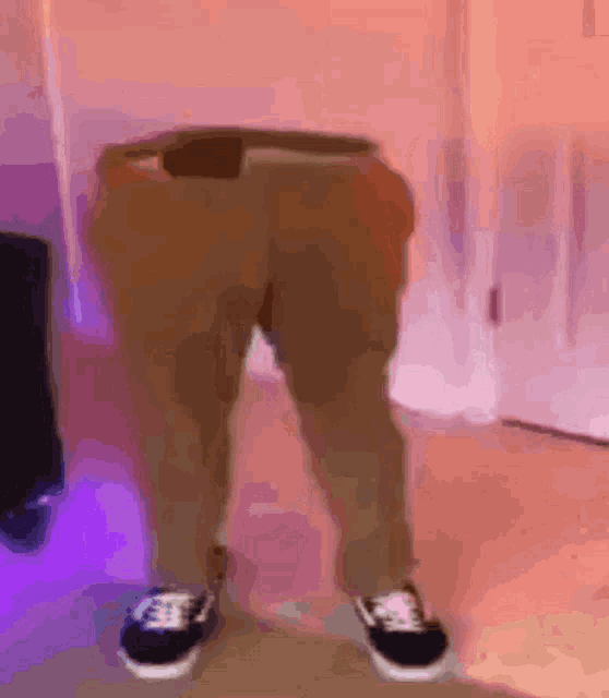 a person wearing a pair of brown pants and black sneakers is standing on a wooden floor .