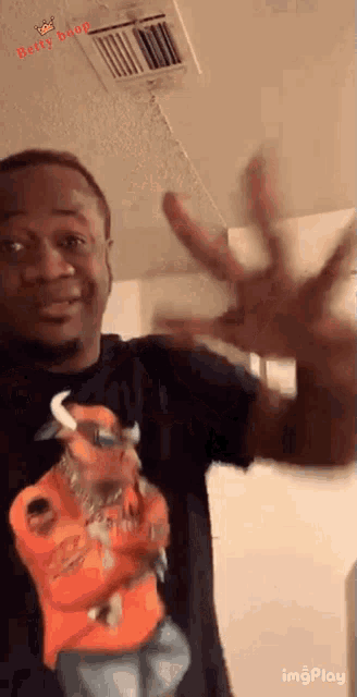 a man wearing a black shirt with a picture of a man in an orange jacket is waving his hand .