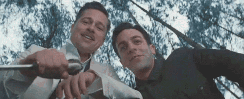 two men are standing next to each other looking up at the camera . one of the men is holding a knife .