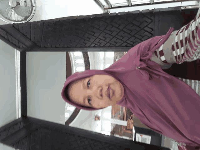 a woman wearing a purple hijab takes a selfie in front of a fan