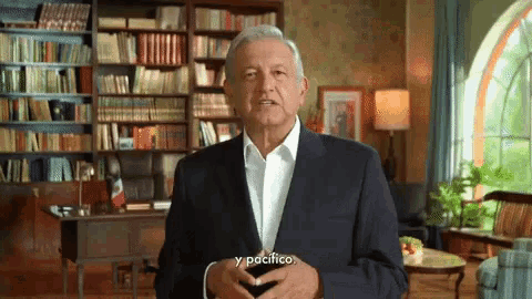 a man in a suit and white shirt is standing in front of a bookshelf and says y pacifico .