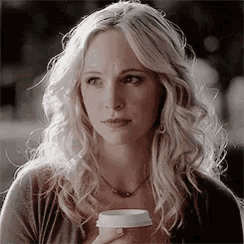 a woman with blonde hair is holding a cup of coffee and looking at the camera .