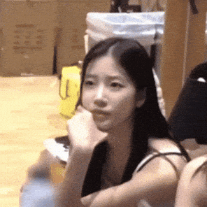 a woman with long black hair is sitting on a wooden floor with a yellow bag in the background