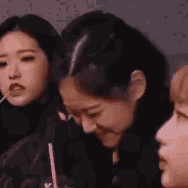 a group of women are sitting next to each other and one of them is holding a pink straw in her mouth .