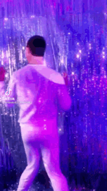 a man is dancing in front of a purple background with purple lights .