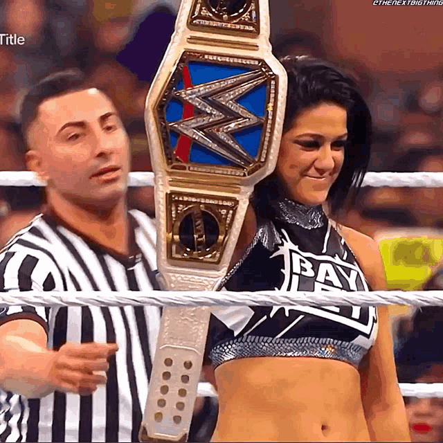 a woman holding a wrestling championship belt with the word bay on her top
