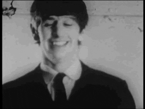 a man in a suit and tie is smiling with his eyes closed in a black and white photo .