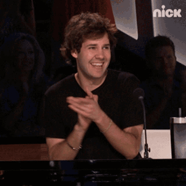 a man applauds while sitting in front of a microphone with the nick logo behind him
