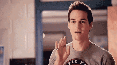a young man wearing a gray t-shirt is waving his hands in a kitchen .