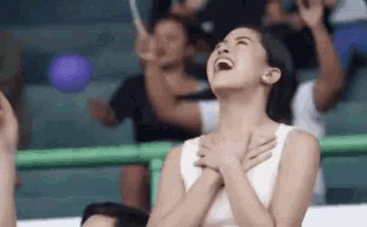 a woman is laughing with her hands on her chest while sitting in a crowd .