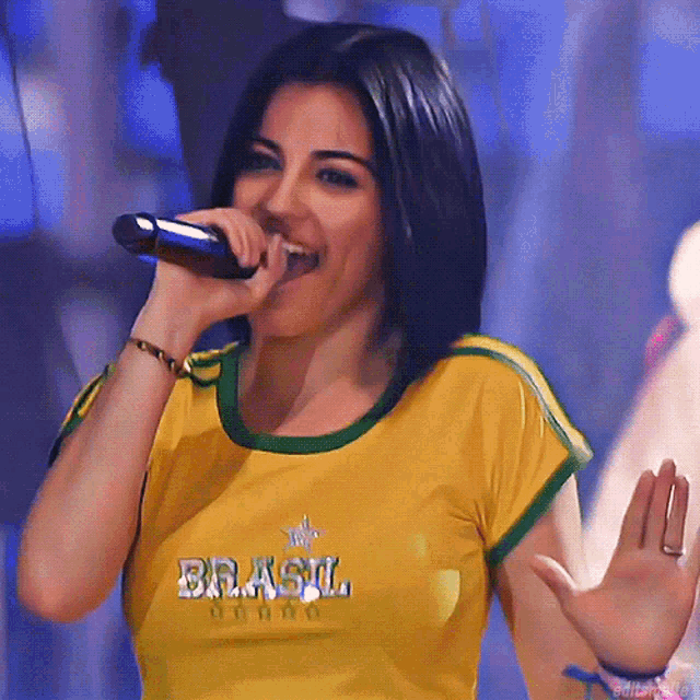 a woman singing into a microphone wearing a shirt that says brasil on it