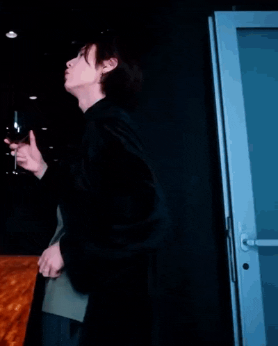 a man in a black coat is holding a glass of wine and standing in front of a door .