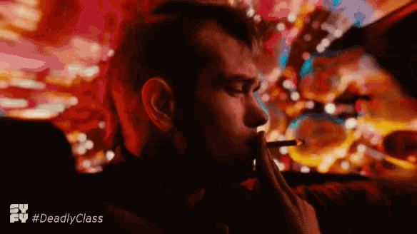 a man is smoking a cigarette and the tv show #deadlyclass is visible in the background