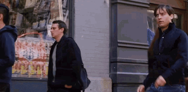 a group of men are walking down a street in front of a store with a sign that says ' a ' on it