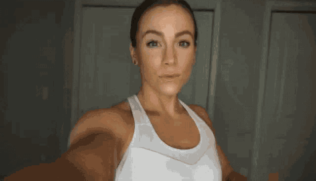 a woman in a white tank top is taking a selfie with her phone .
