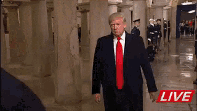 a man in a suit and tie is walking down a hallway with a live sign behind him .