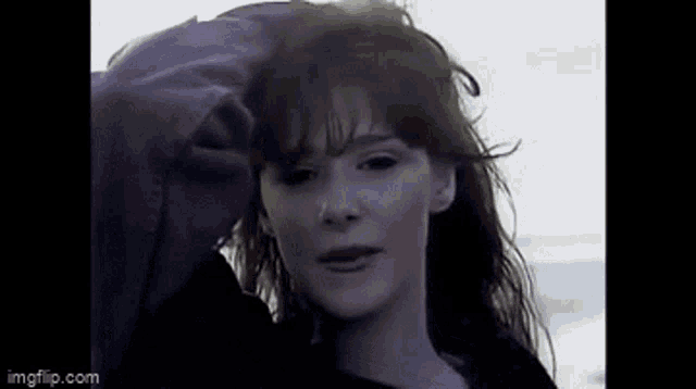 a close up of a woman 's face with her hand on her hair .