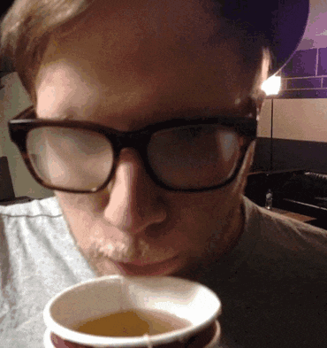 a man wearing glasses is drinking from a cup of coffee